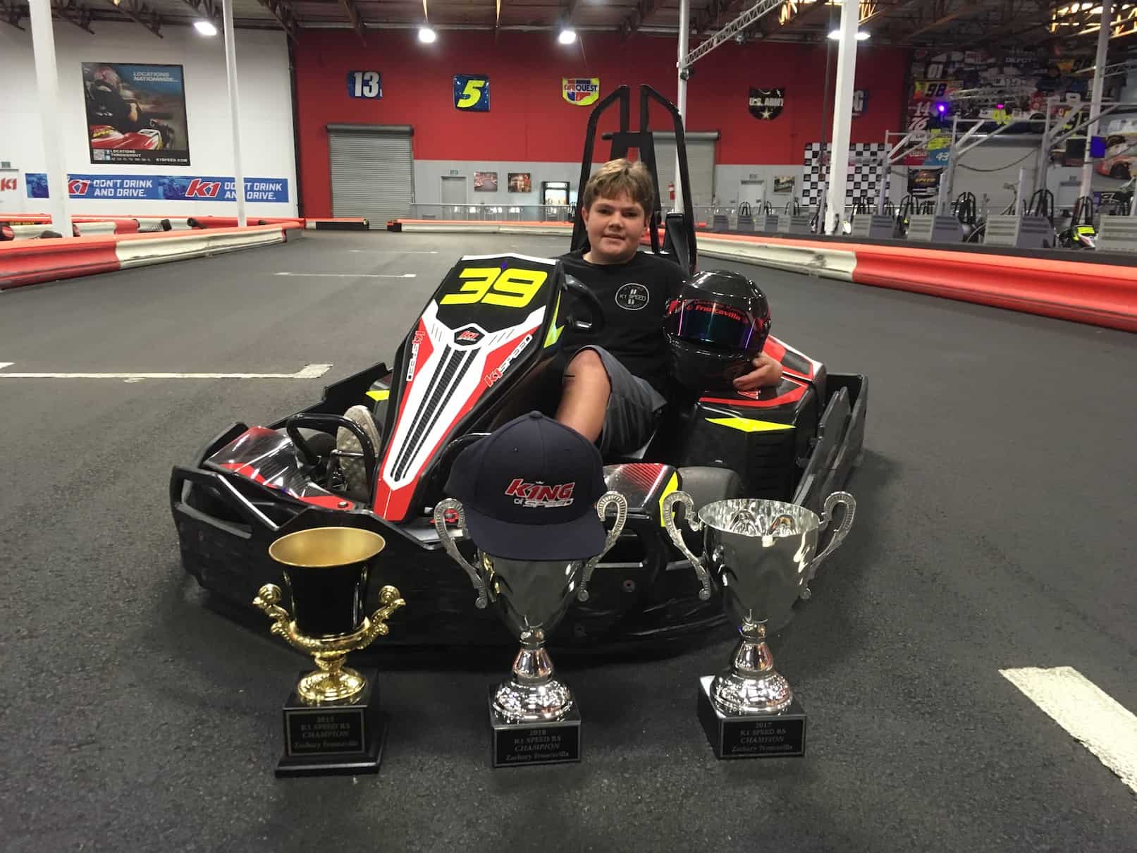 Zachary Francavilla sits in a gokart at K1 Speed surrounded by his trophies