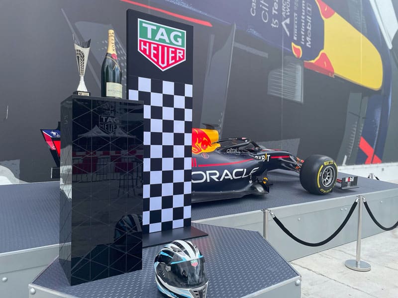 a podium at the outdoor kart track with a tag heuer k1 speed helmet, trophy, champagne, and a f1 car
