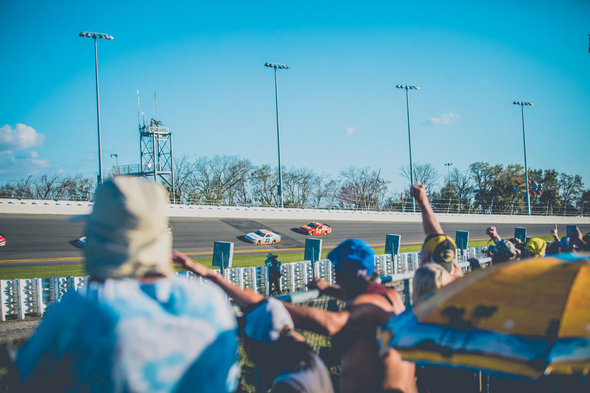 a crowd cheers as stock cars race by at daytona international speedway