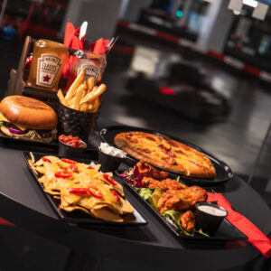 cheeseburger, fries, pizza, nachos, and wings sit on a table overlooking the karting track at k1 speed canary wharf in london