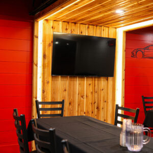 A TV hangs on a wall in front of a long table with chairs inside the party room at K1 Speed Oxford