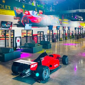 A race car positioned next to some couches, with a view of the track.