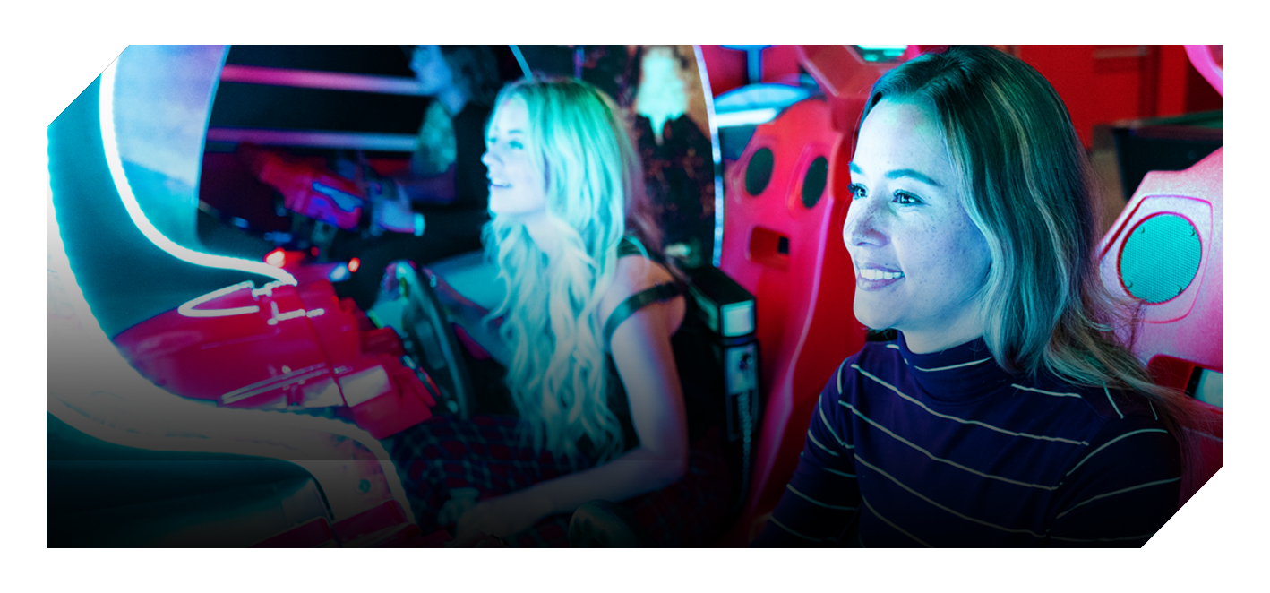 Two guests smiling while playing an arcade racing game at K1 Speed.